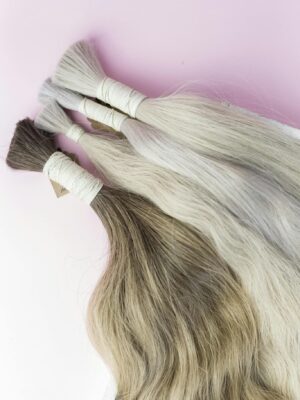 Close-up view of diverse human hair extensions on a soft pink surface.