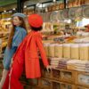 Two stylish women in a market showcasing fashion amidst colorful spices and grains.