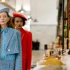 Two stylish women standing at a spice stall in an indoor market, exuding elegance