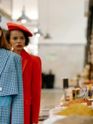 Two stylish women standing at a spice stall in an indoor market, exuding elegance