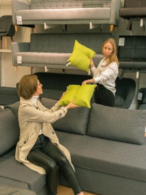 Two women choosing green cushions in a modern furniture store, enjoying shopping.